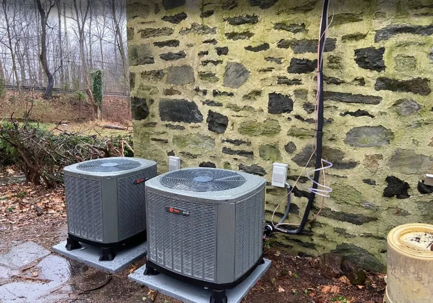 Two heat pump outdoor units beside an older stone house