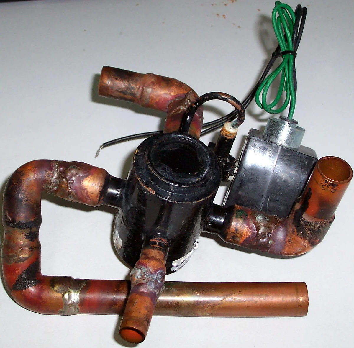 A heat pump reversing valve removed for inspection, with its solenoid coil and copper stubs